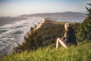 woman sat in grass on edge of cliff on coast